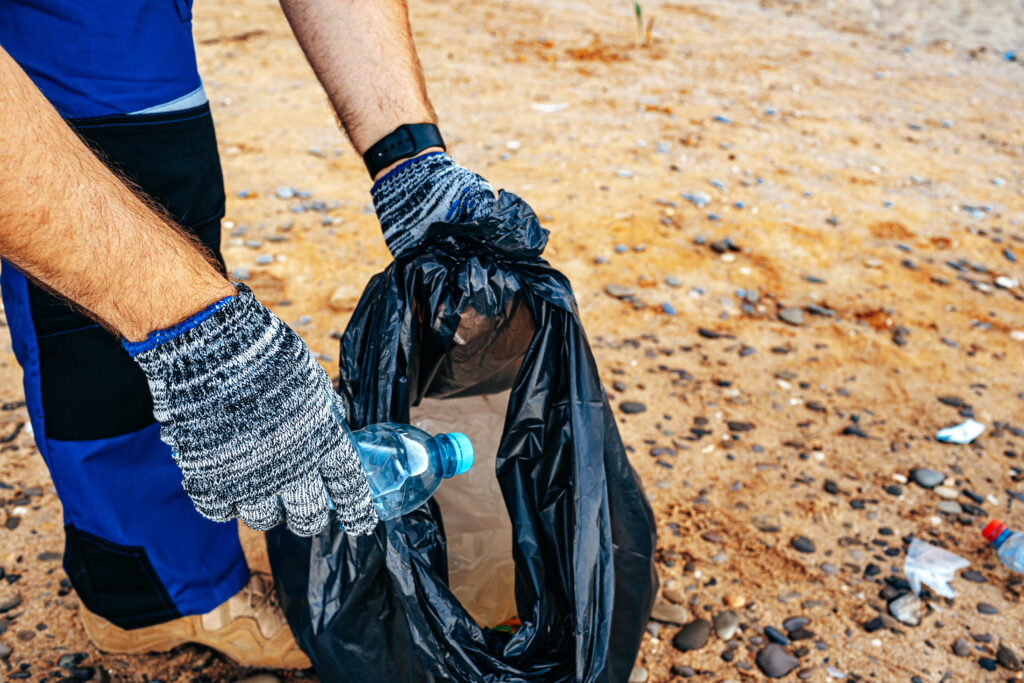 Hand of a man volunteer grabbing plastic litter into a waste bag cleaning up the beach